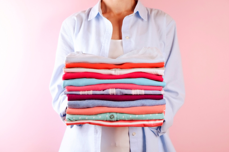 Female holding a pile of folded clothes, unisex for both man & woman, different color & material. Trip preparation concept.